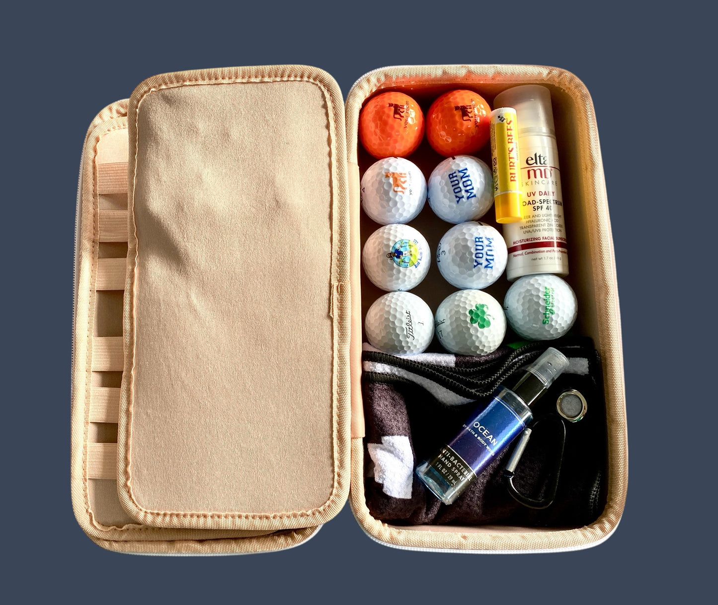 Open beige case containing golf balls, oranges, and other items on a dark background